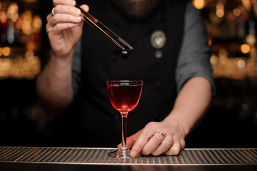 Bartender adding a one red berry with tweezers to the cocktail