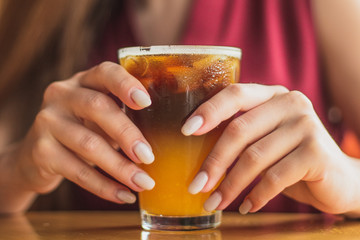 Close up of glass with black orange coffee in female hand, cold coffee cocktail recipe idea. Selective focus