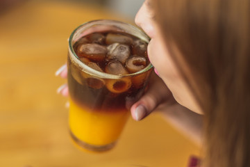 beautiful girl holds a glass of cold coffee mixed with ice and orange juice on cafe background. Selective focus