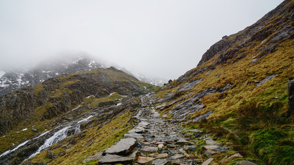 Stunning landscape with foggy skies, melting ice and rugged road among beautiful mountains – captured during a hike at Snowdon in winter (Snowdonia National Park, Wales, United Kingdom)