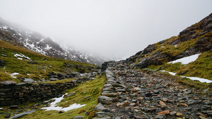 Stunning landscape with foggy skies, melting ice and rugged road among beautiful mountains – captured during a hike at Snowdon in winter (Snowdonia National Park, Wales, United Kingdom)