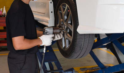 Mechanic man with impact wrench tool changing tires of car in car auto service shop