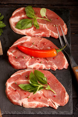 Raw pork meat steak with vegetables, salt, rosemary and spices cooking over stone table. Top view.