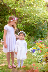 Fototapeta premium Outdoor portrait of two cute little girls. Beautiful children witn white dresses and flower wreath on colorful nature background.