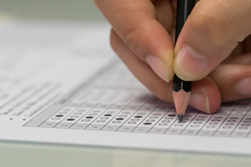 Student hand filling out in answer sheet with standardized test form. - obrazy, fototapety, plakaty