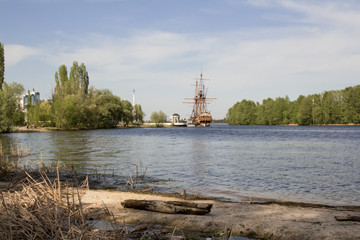 Cityscape, wide river, beautiful embankment, old wooden ship.  City in the distance, across the river.