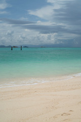View from the beach on wooden piles in crystal clear sea water over boats and cloudy sky background