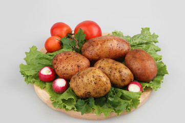 Lots of raw potatoes on wood board with radish, tomatoes, oak lettuce, on gray isolated background