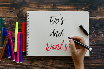 Top view of colorful pen and hand holding black pen writing Do's and Dont's on notebook on wooden...