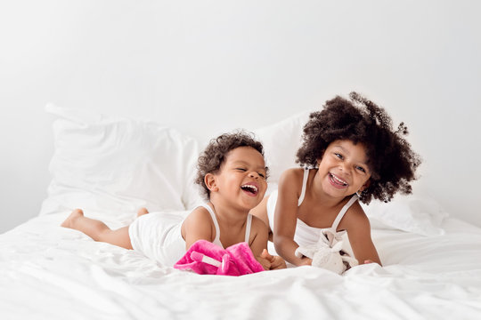 Two little girls laughing together on white bed