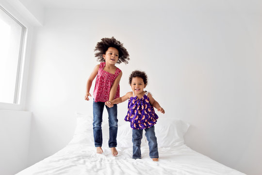 Little girl with afro hair and her baby sister jump on bed