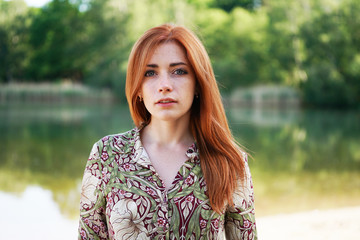 cool and confident young woman wearing floral pattern summer dress with long red hair standing by...