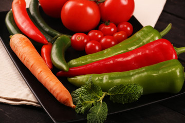 Vegetables, peppers, tomato, carrot, rosemary and spices over black plate and table.