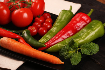 Vegetables, peppers, tomato, carrot, rosemary and spices over black plate and table.