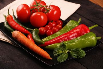 Vegetables, peppers, tomato, carrot, rosemary and spices over black plate and table.