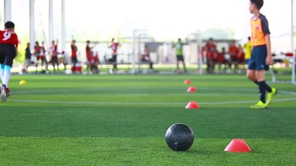 black football on green artificial turf with marker cone blurry soccer team training, blurry boy soccer player jogging between marker cones and control ball with soccer equipment in soccer academy. - Powered by Adobe