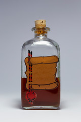 A vintage medicine bottle with cork filled with orange liquid and furnished with an empty label designed like a parchment roll with red sealing wax. Arrangement on white background.