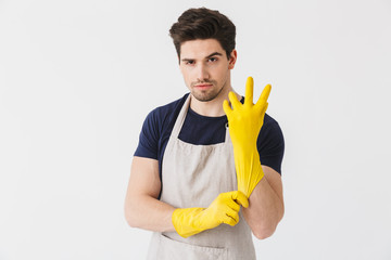 Image of brunette young man wearing yellow rubber gloves for hands protection looking at camera while cleaning house