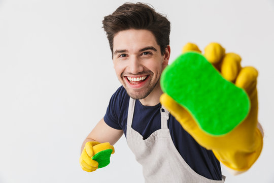 Photo of optimistic young man wearing yellow rubber gloves for hands protection holding sponges while cleaning house