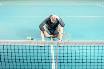 male tennis player sitting on the court. athlete holding a racket. sportsman has adjusted, lost and holds his head.