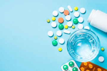 Pills and glass of water on blue top view.