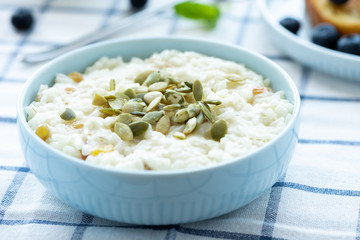 Sweet rice porridge, pudding, with raisins and pumpkin seeds in a blue bowl on the table. Delicious country breakfast.