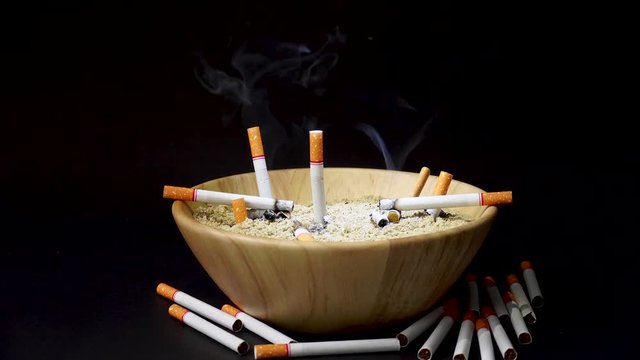 Many cigarettes are placed in a wooden cup of sand on a black background.