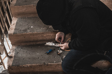Young man addict with a syringe and heroin in the dirty basement (stairs). Drug addict. social issue