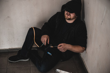 Young man addict with a syringe and heroin in the dirty basement (stairs). Drug addict. social issue