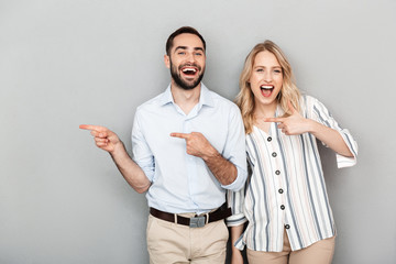 Photo of happy couple in casual clothing smiling while pointing fingers aside at copyspace