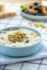 Sweet rice porridge, pudding, with raisins and pumpkin seeds in a blue bowl on the table. Delicious country breakfast.