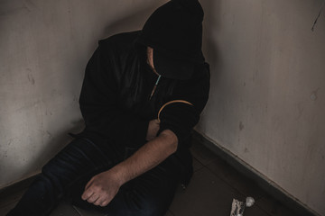 Young man addict with a syringe and heroin in the dirty basement (stairs). Drug addict. social issue