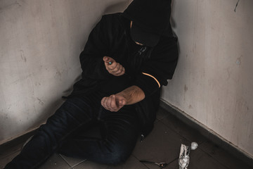 Young man addict with a syringe and heroin in the dirty basement (stairs). Drug addict. social issue