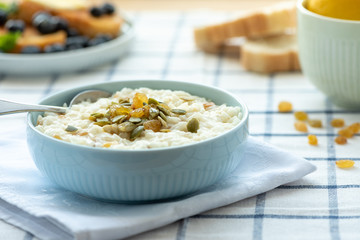 Sweet rice porridge, pudding, with raisins and pumpkin seeds in a blue bowl on the table. Delicious country breakfast.