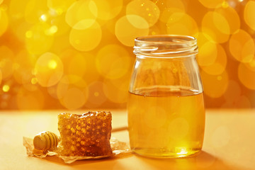 Jar with honey and fresh comb on table against blurred background