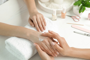 Cosmetologist applying cream on woman's hand at table in spa salon, closeup