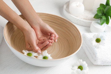 Woman soaking her hands in bowl of water and flowers on table, closeup with space for text. Spa treatment