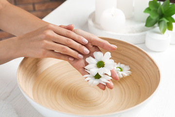 Fototapeta na wymiar Woman soaking her hands in bowl with water and flowers on table, closeup. Spa treatment