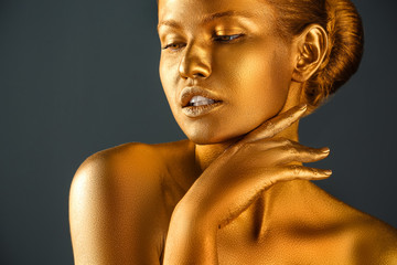 Portrait of beautiful lady with gold paint on skin against grey background, closeup