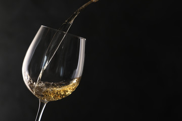 Pouring white wine into glass on dark background. Space for text