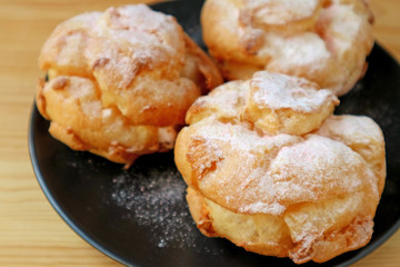 Closeup French Cream Puffs on Black Plate Sprinkled with Icing Sugar
