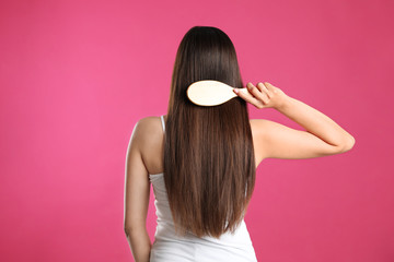 Back view of young woman with hair brush on color background