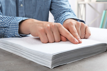 Blind person reading book written in Braille at table, closeup