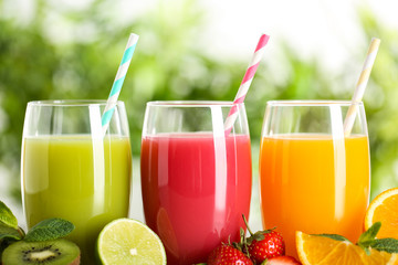 Glasses of different juices with straws and fresh fruits on blurred background