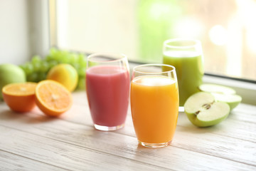 Glasses with different juices and fresh fruits on wooden window sill