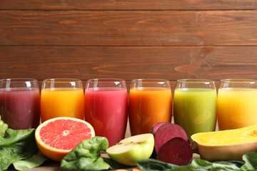 Glasses with different juices and fresh ingredients on wooden background
