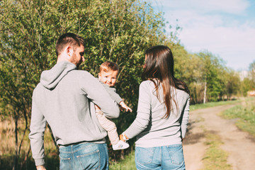 Happy family with cute baby boy walking on road outdoors, sensitivity to nature concept