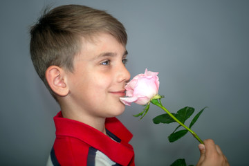 The boy holds a rose in his hand and sniffs it, the concept of love and celebration and celebration.