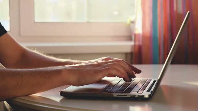 Close-up hands of a male outsourcing employee work at home with a laptop while sitting at a table in his office. Freelance work concept