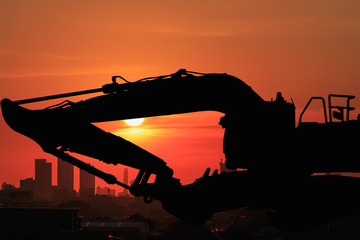 Silhouette of Excavator in cityscape background with twilight sunset in bangkok